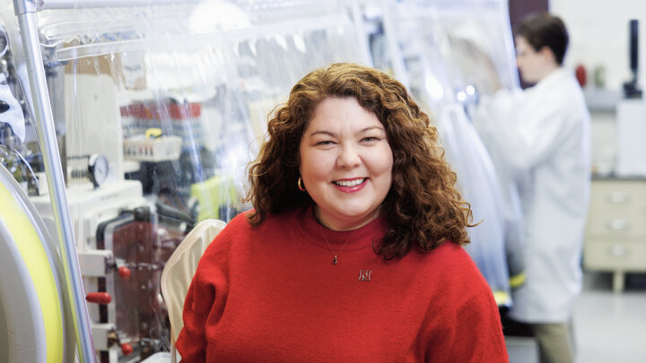 Nicole Buan, a white woman with curly red hair, smiles in a lab in a red sweater.